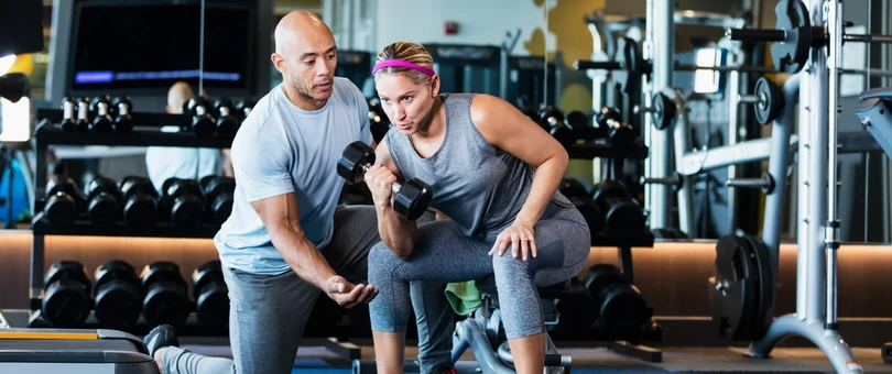 athletic trainer helping woman list dumbbell